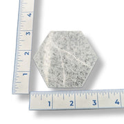A hexagonal selenite charging plate with a textured, speckled gray and white surface, shown with two metal rulers on a white background to indicate its size.