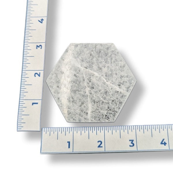 A hexagonal selenite charging plate with a textured, speckled gray and white surface, shown with two metal rulers on a white background to indicate its size.