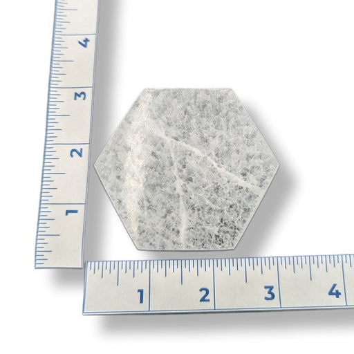 A hexagonal selenite charging plate with a textured, speckled gray and white surface, shown with two metal rulers on a white background to indicate its size.