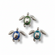 Three sea turtle jewelry charms in silver-tone metal with green, blue, and teal enamel fills, arranged on a white background.
