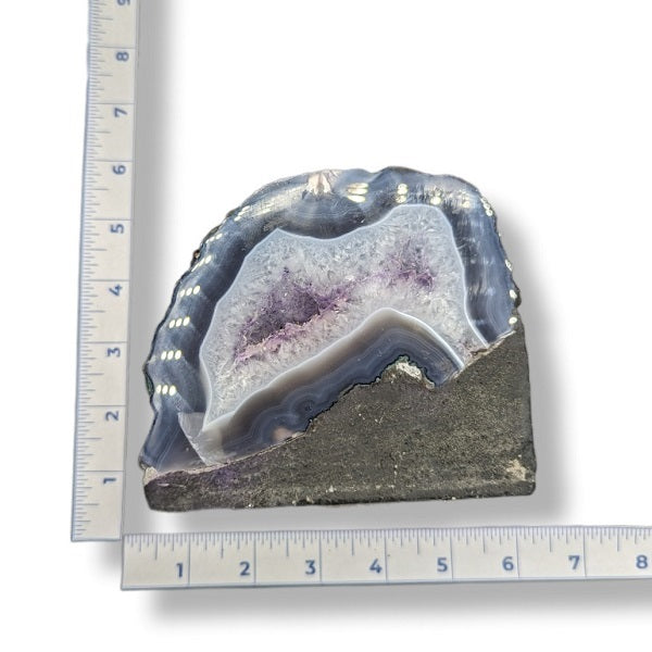 Geode with purple interior on a white background with a ruler for scale.
