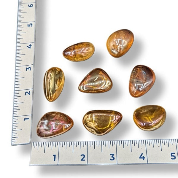 Tangerine aura tumbled crystals on a white background with a ruler for size.
