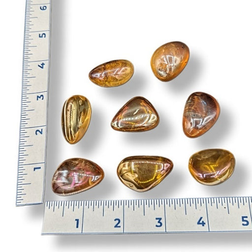 Tangerine aura tumbled crystals on a white background with a ruler for size.