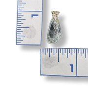 Teardrop-shaped pendant next to a ruler for scale on a white background