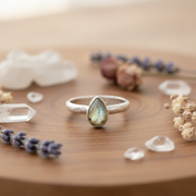 Silver ring with a teardrop-shaped gemstone on a table with herbs and crystal around decoratively