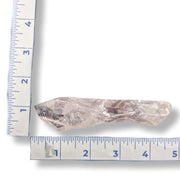 A rough, translucent pale pink crystal or gemstone shown on a white background with blue measurement rulers along the left and bottom edges for size reference.