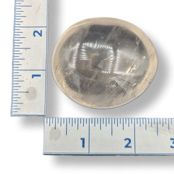 Circular girasol quartz tumbled  next to a ruler on a white background