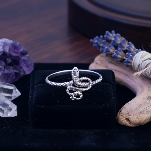 Silver snake-shaped ring on a black box with decorative elements like lavender and crystals.