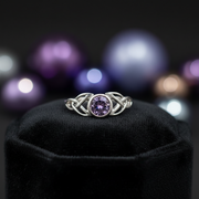Silver ring with a purple gemstone on a black stand against a blurred multicolored background