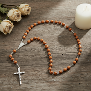 Wooden rosary with a silver cross on a wooden surface with roses and a candle.