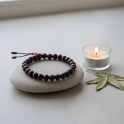 Meditation bracelet on a stone with a lit candle and leaves on a light surface