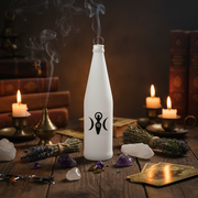 White bottle with a black symbol on a wooden table with candles and crystals