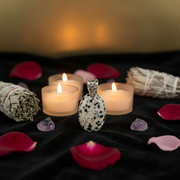 Decorative setting with candles, a pendant, crystals, and rose petals on a dark surface.