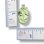 Green stone pendant with silver setting next to a ruler for scale on a white background