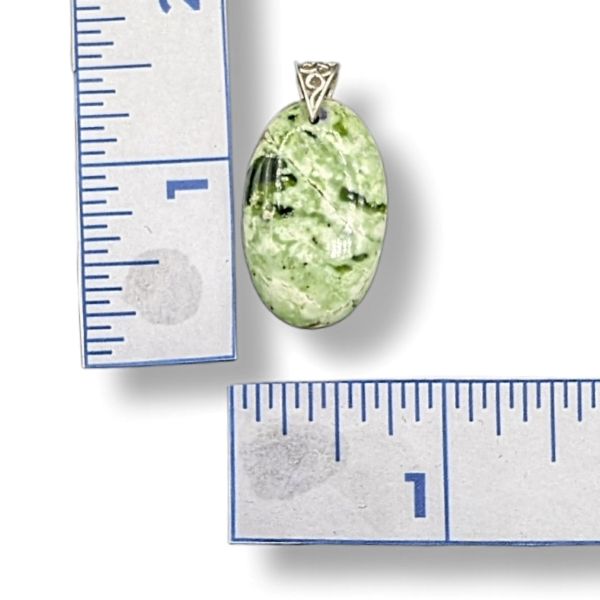 Green stone pendant with silver setting next to a ruler for scale on a white background