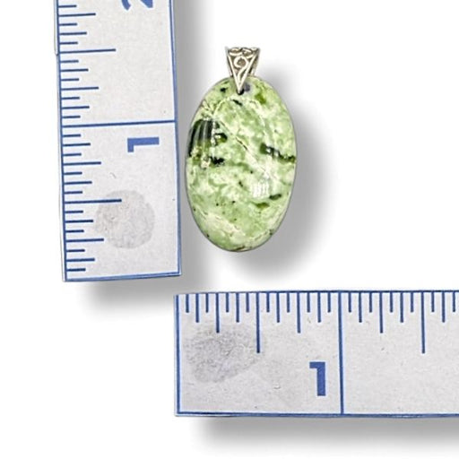 Green stone pendant with silver setting next to a ruler for scale on a white background