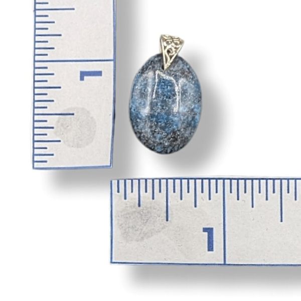 Blue stone pendant with sterling silver setting next to a ruler for scale on a white background