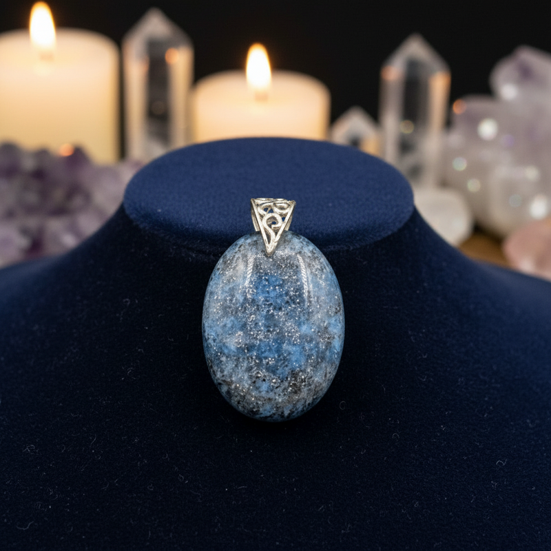 Blue stone pendant with silver triangle design on a blue stand, candles, and crystals in the background