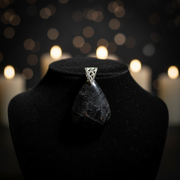 Jewelry display with a dark purple stone pendant on a black stand against a dark background with blurred lights.