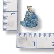 Blue stone pendant with silver setting on a white background with rulers for scale.