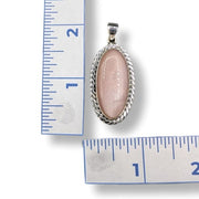 Pink stone pendant with silver frame on a white background with ruler for scale