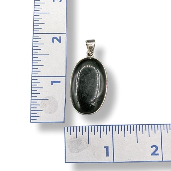 Black oval pendant with silver setting on a white background with rulers for scale.