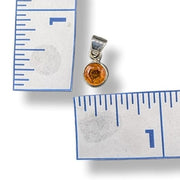 Silver pendant with a round orange gemstone next to a ruler for scale on a white background