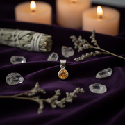 Silver pendant with a yellow gemstone on a purple fabric background with candles and crystals.