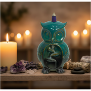 Teal owl-shaped incense burner with a lit candle and crystals on a wooden surface.