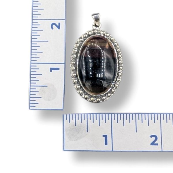 Silver pendant with a dark purple stone next to a ruler for scale on a white background