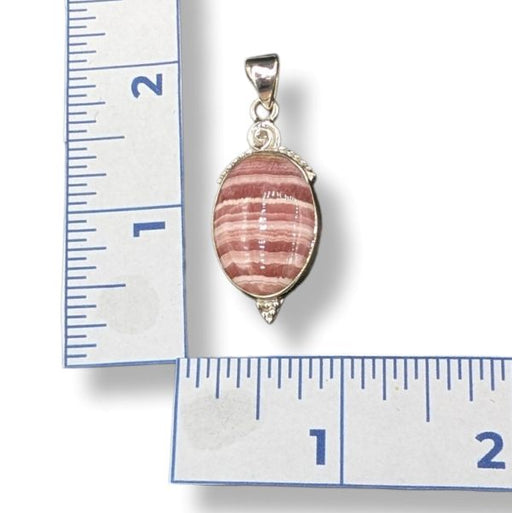 Pink and silver pendant on a ruler for scale
