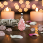 Pink teardrop pendant on a wooden surface with candles and crystals in the background