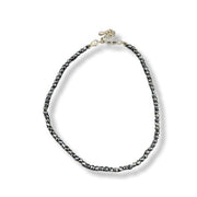 A beaded anklet featuring dark gray to black round beads with a polished gold-tone clasp and extender chain, displayed on a clean white background.