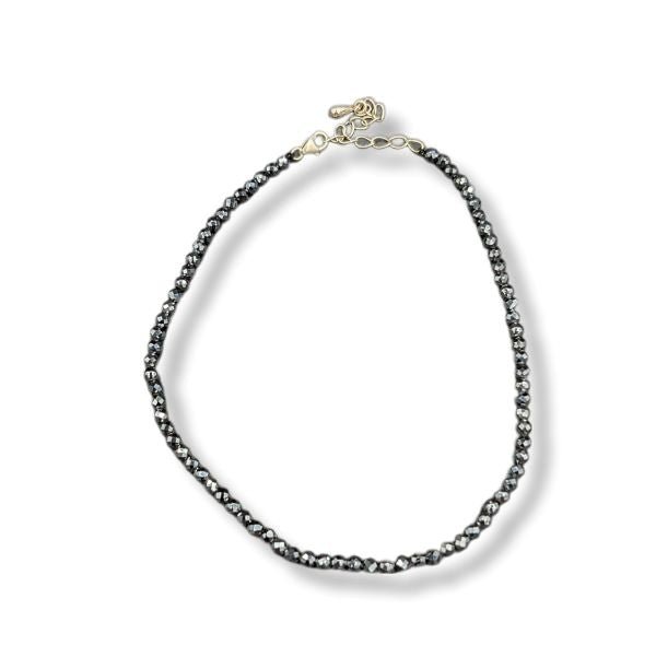 A beaded anklet featuring dark gray to black round beads with a polished gold-tone clasp and extender chain, displayed on a clean white background.