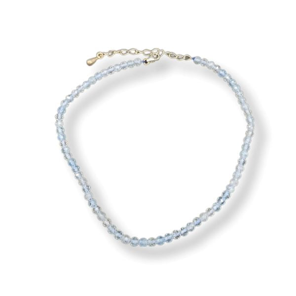 A delicate beaded anklet with light blue faceted beads and a gold-tone clasp, displayed on a clean white background.