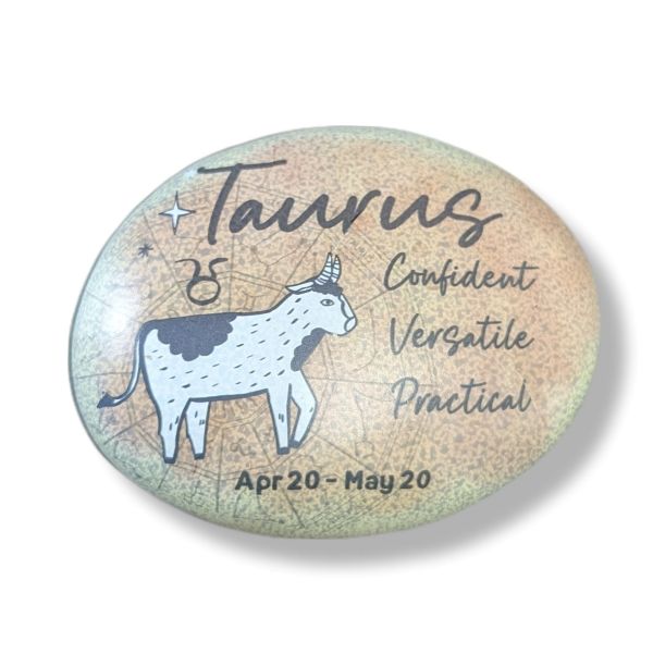 Round stone with Taurus zodiac design, cow illustration, and descriptive text on a light background