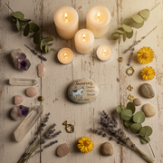 Candles, stones, crystals, and flowers arranged on a wooden surface with a Taurus art stone in the middle