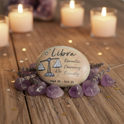 Decorative stone with Libra zodiac sign on a wooden surface with candles and lavender.