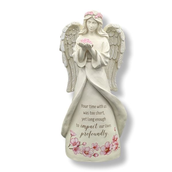 An angel figurine statue in an off-white/cream color, featuring pink flowers on its head and waist, holding pink flowers in its hands. The statue has a printed memorial quote on the front and is set against a plain white background.