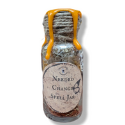 Small glass jar with a label reading 'Needed Change Spell Jar' on a white background