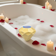 Gold diamond-shaped bar of soap in a bathtub with candles and rose petals