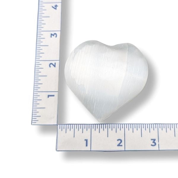 Heart-shaped selenite next to a ruler on a white background
