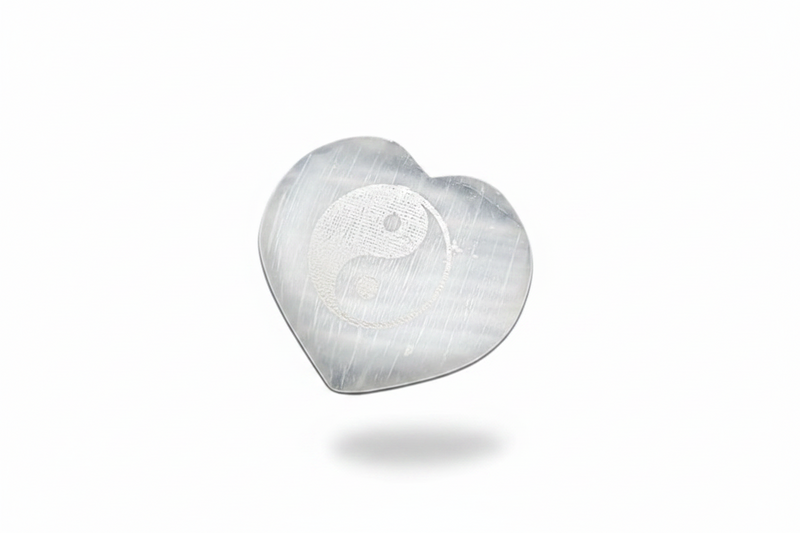 A selenite heart with a etched yin yang, on a white background