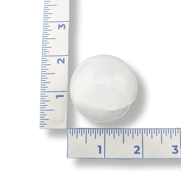 White spherical selenite next to a ruler on a white background