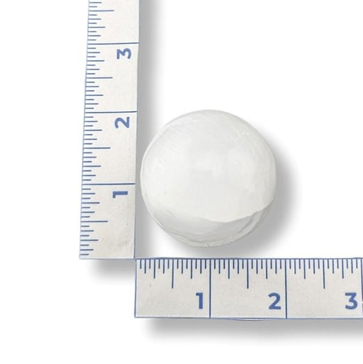 White spherical selenite next to a ruler on a white background