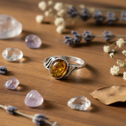 Silver ring with a amber stone on a wooden surface with gemstones and flowers.