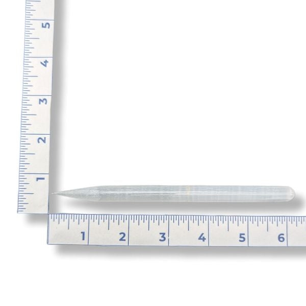 A selenite pencil wand with a ruler for measurement on a white background