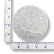 Round selenite charging plate with a ruler for scale on a white background