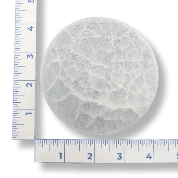 Round selenite charging plate with a ruler for scale on a white background