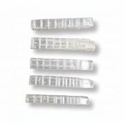 Five selenite sticks with a ribbed texture, arranged vertically on a white background with soft drop shadows.